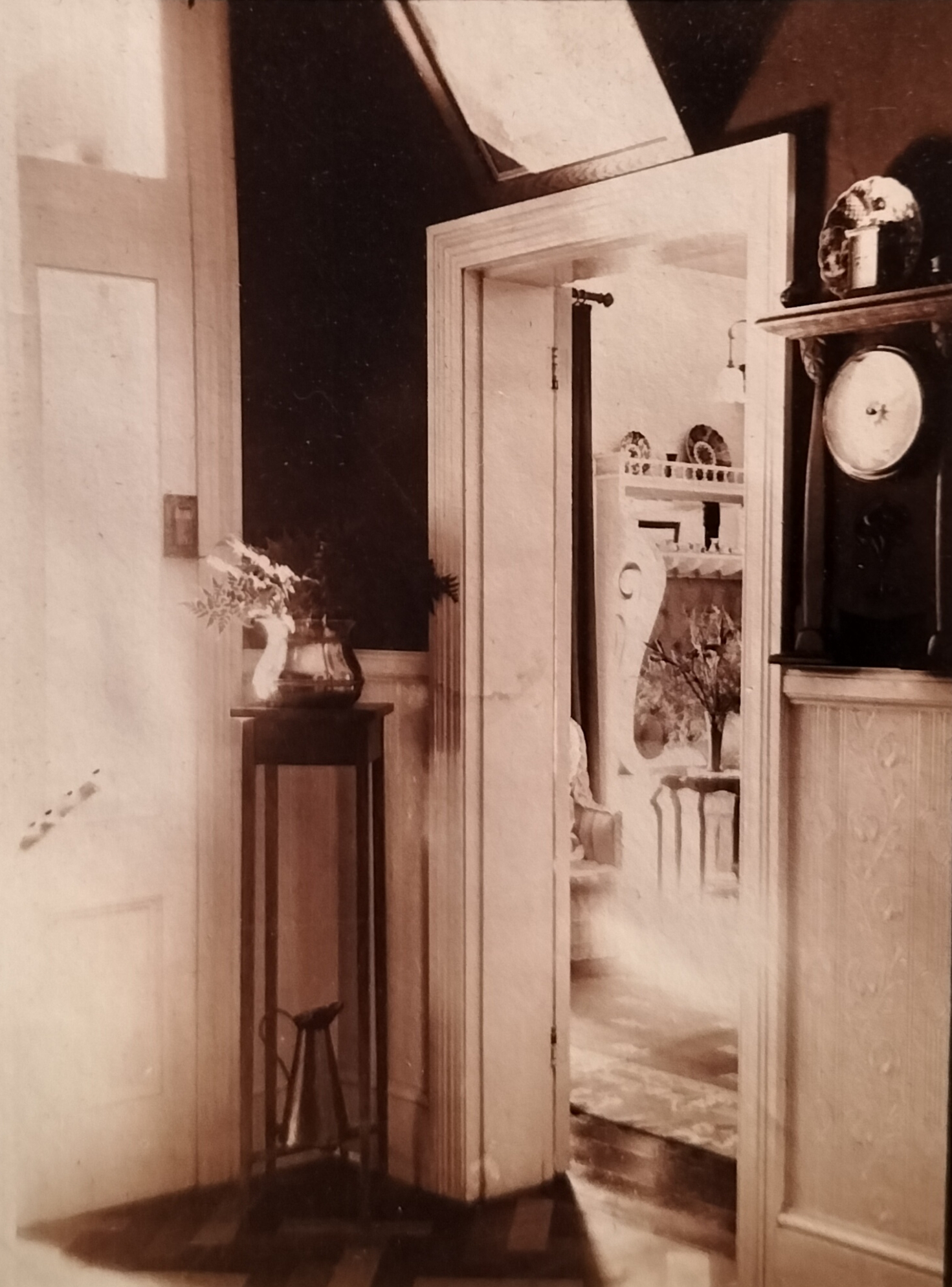 Looking into the music room from the entrance hall with the front door and a clock or thermometer visible. At the back, a bench can be seen which is more visible in another photograph further down.