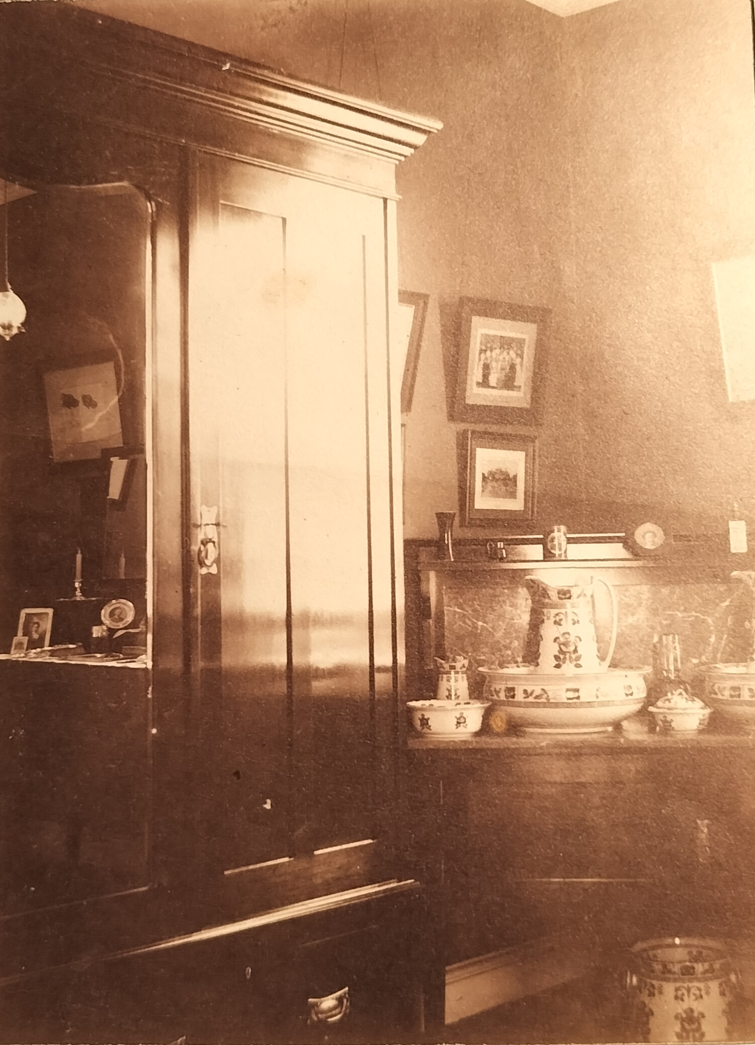 The opposite side of the room with the washstand as well as large wooden cabinet. Note the family photographs as well as dog picture reflecting in the mirror